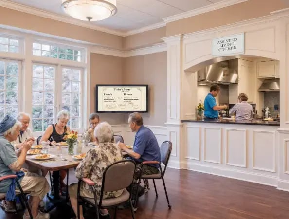 Digital menu board at a senior facility center with a kitchen in the background and seniors eating dinner in the foreground