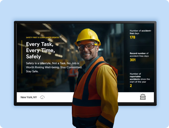 A male wearing a hard hat and safety goggles stands in front of a digital display showing digital signage for safety