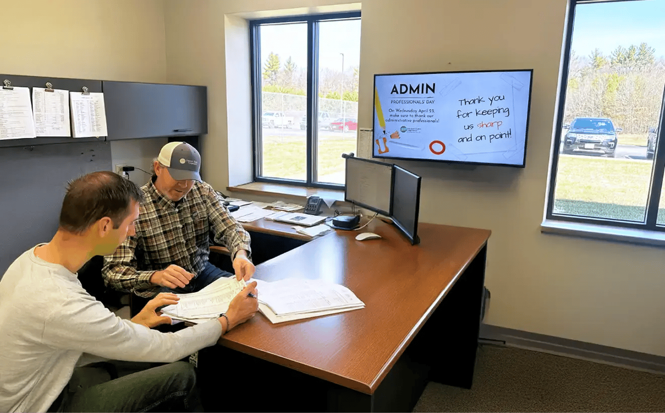 Two colleagues in an office room viewing documentation with a digital signage display mounted in the office