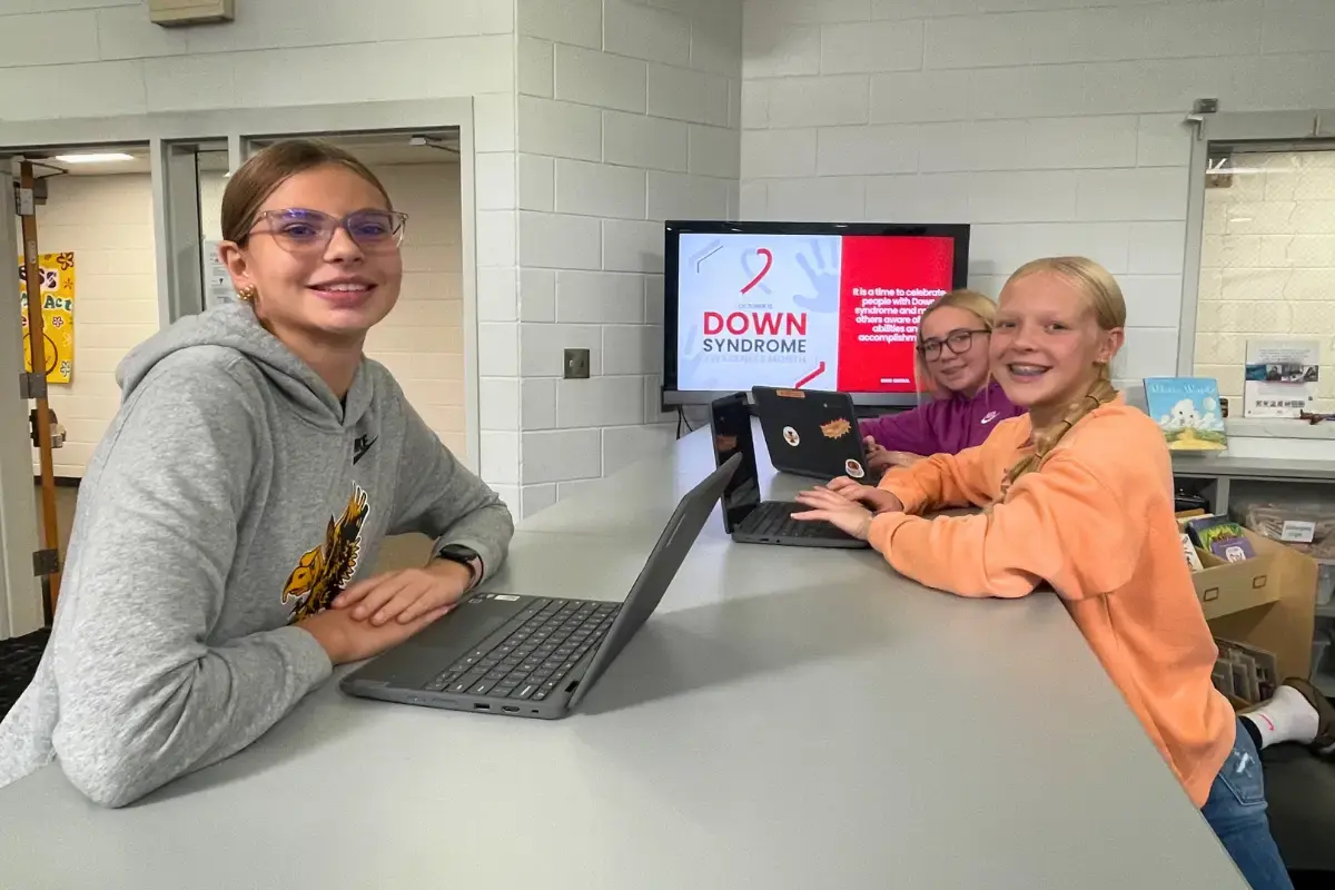 Female students using their laptops with a digital signage display in the background