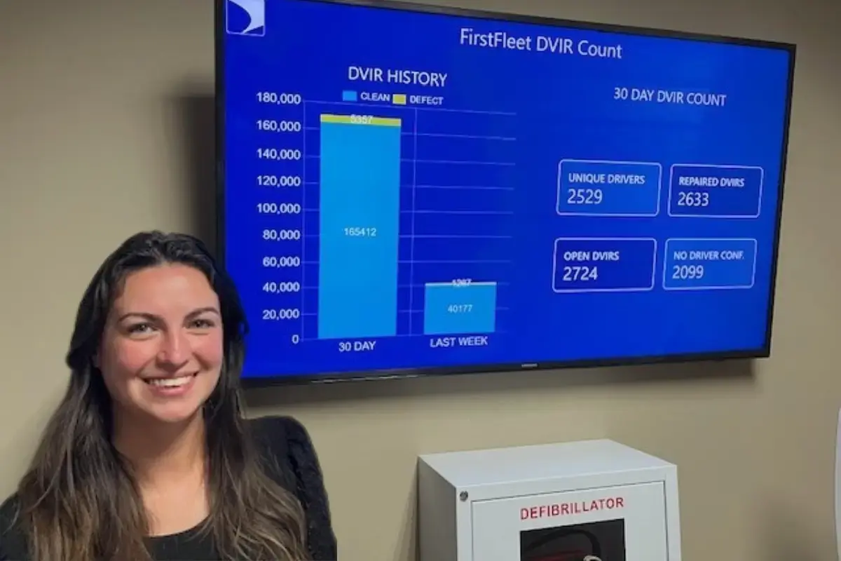A female fleet employee standing in front of digital signage display with DVIR history