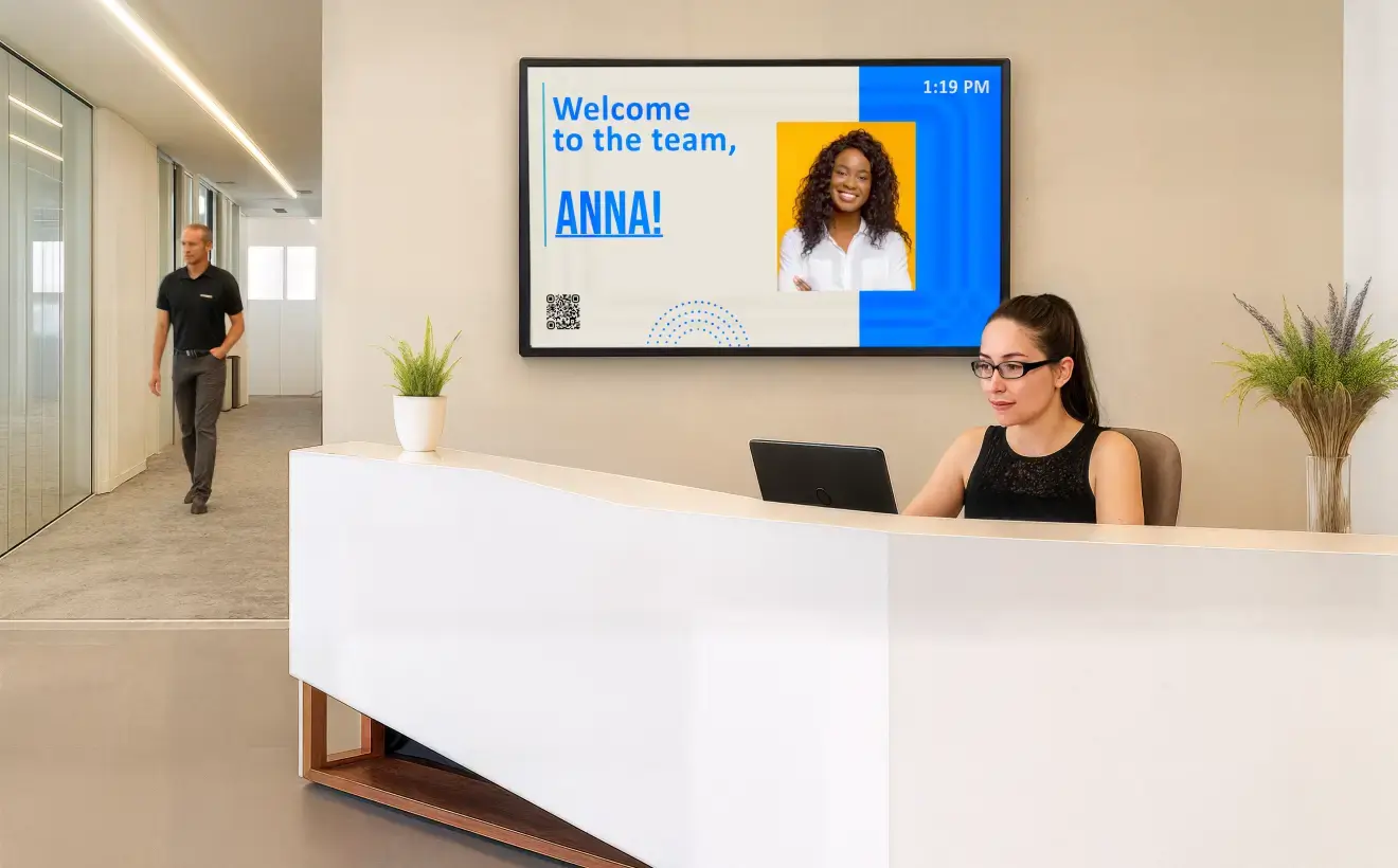 An office receptionist at her desk with a large digital signage display in the background