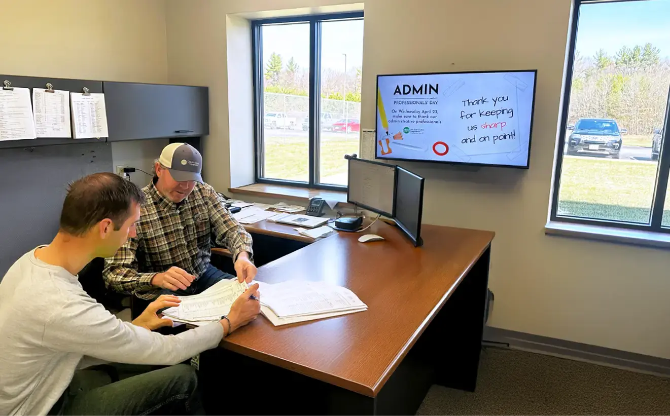Two colleagues in an office room viewing documentation with a digital signage display mounted in the office