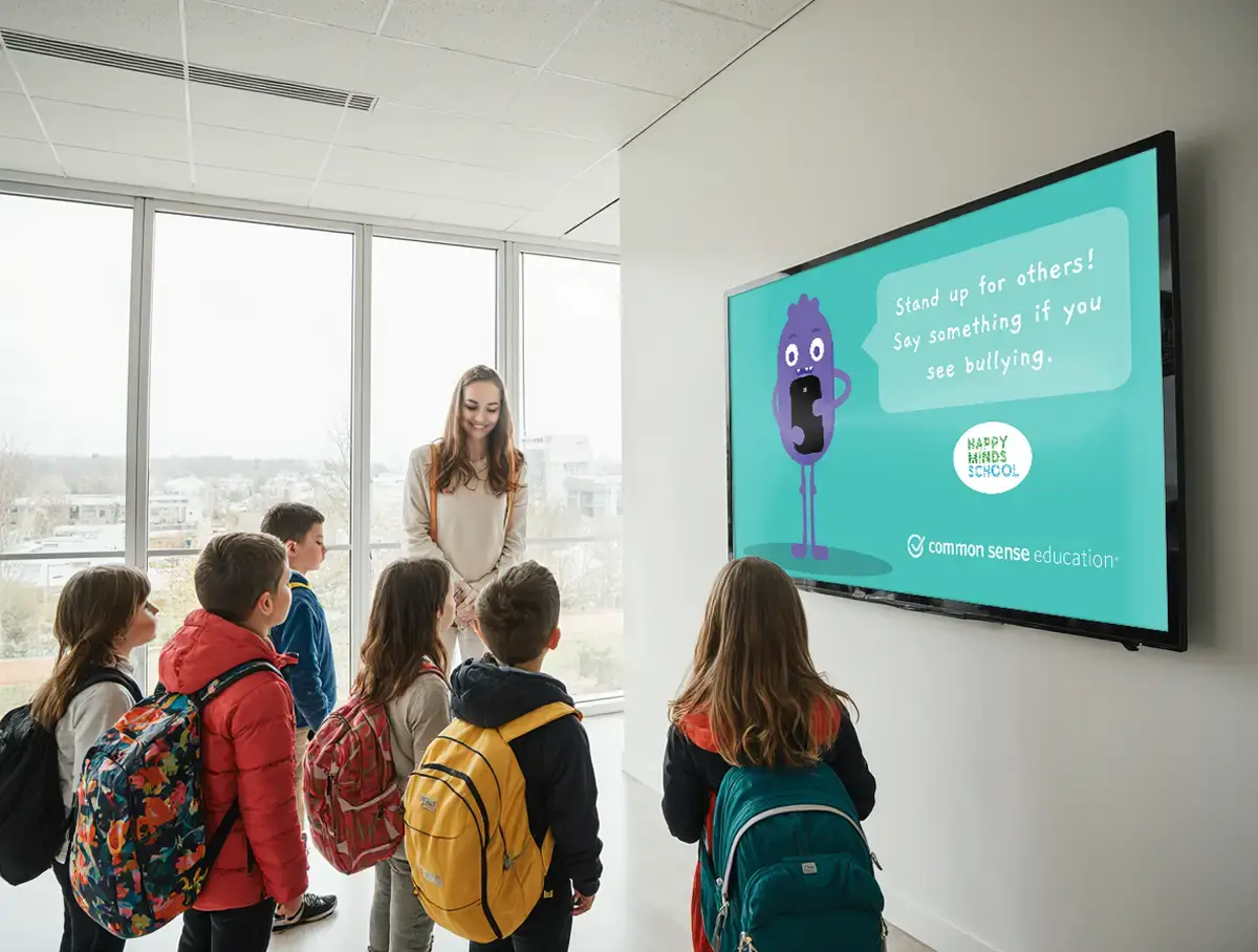 A group of students and a teacher standing in a school hallway viewing a Rise Vision digital display