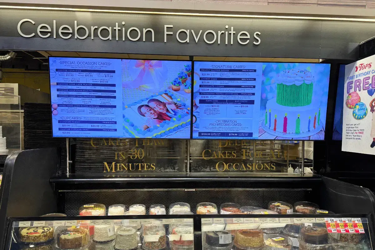 Digital menu boards near a restaurant refrigerator with cakes