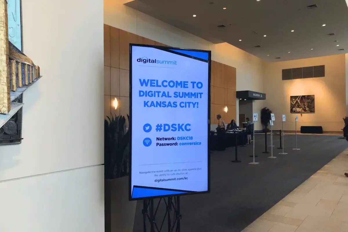 A large digital signage display in the interior of a digital summit conference
